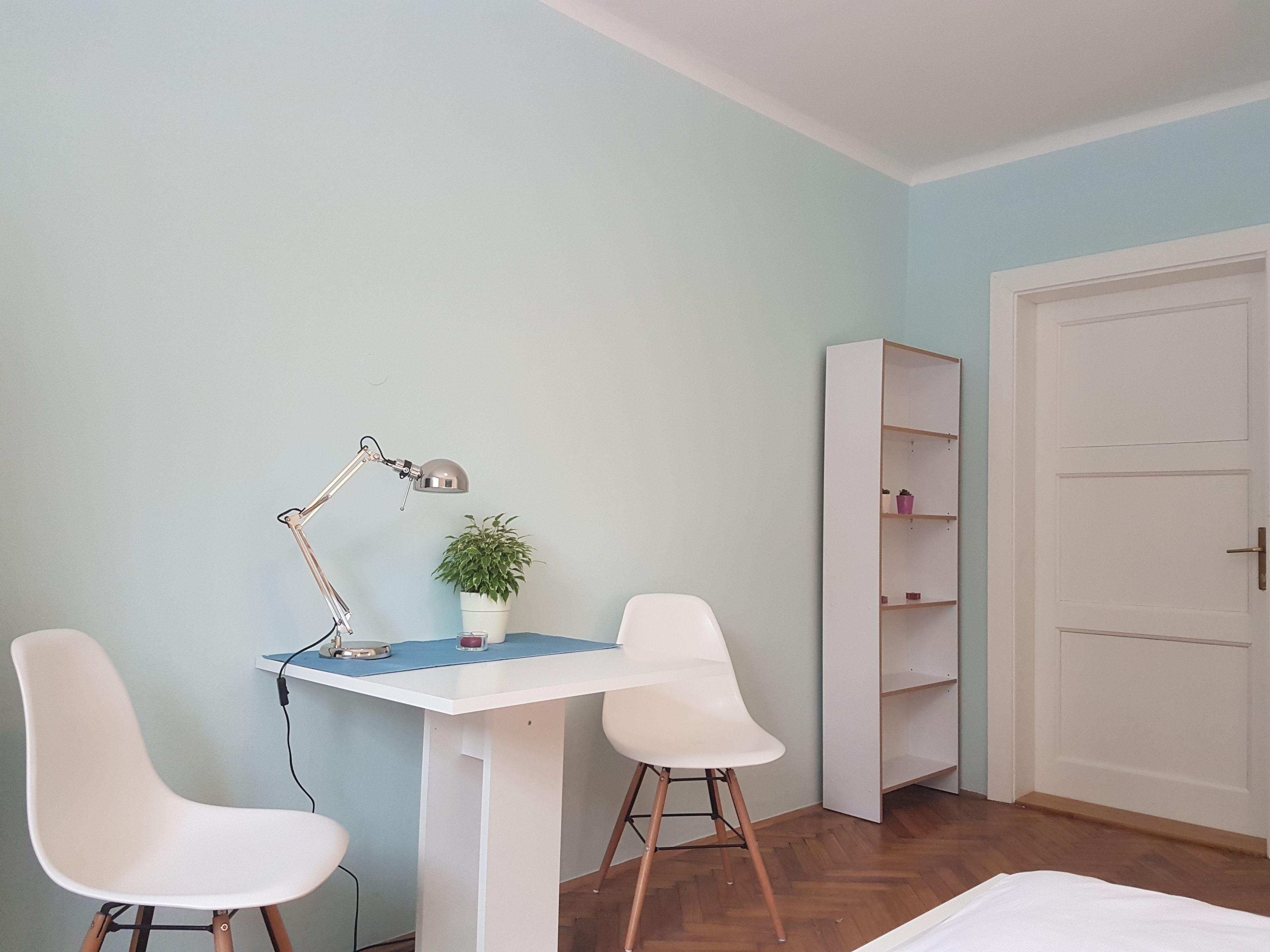 A room with a white desk, two white chairs, a small potted plant, and a white bookshelf.