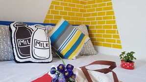 Una habitación con un mural de pared ladrillo amarillo, suelo rojo y sofá blanco con cojines estampados.