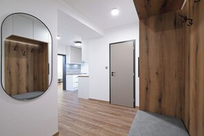 A hallway with a wooden panel wall, a round mirror, a door, and a bench. -  Carlsbad INN hotel & apartments (Dalovice)