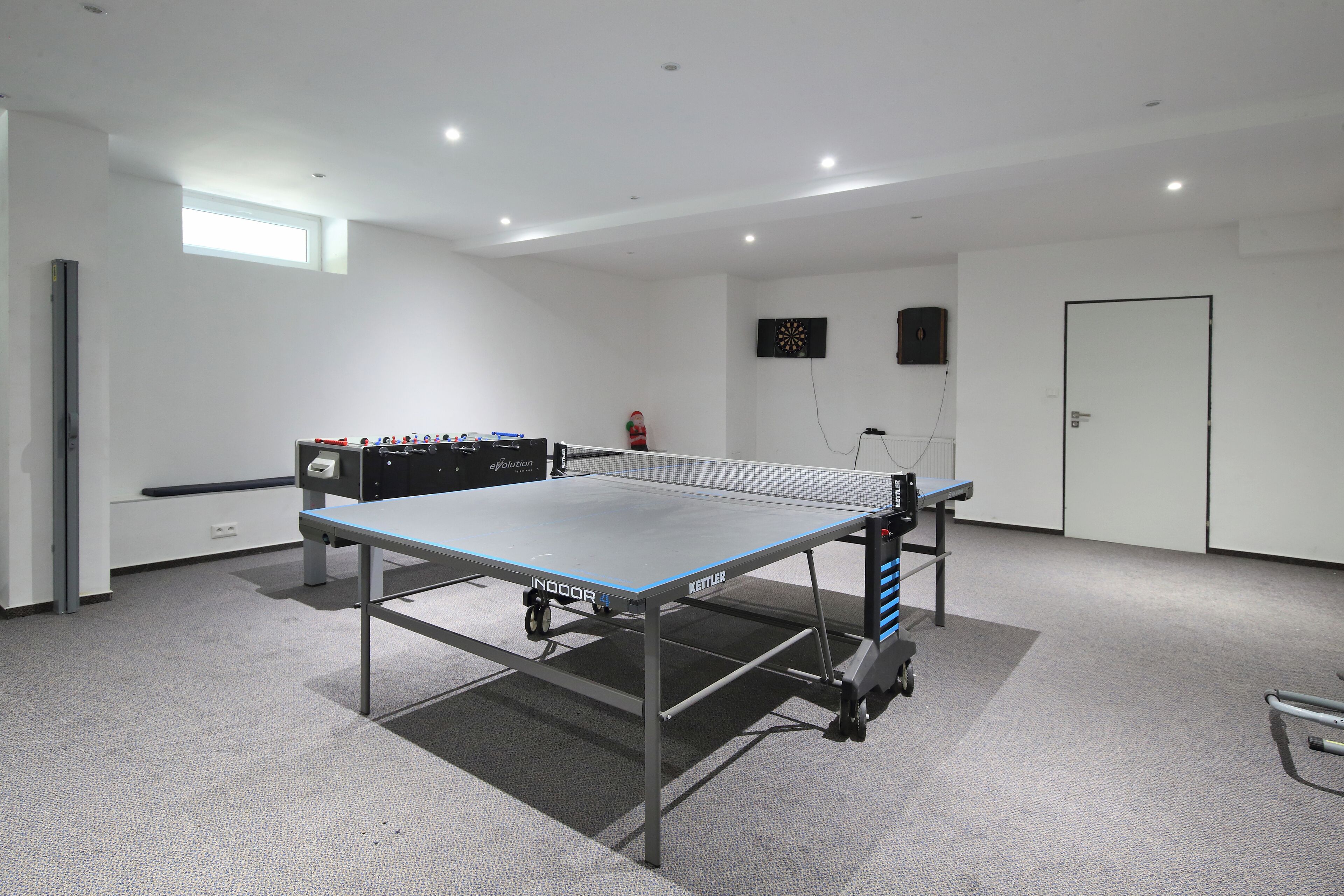 A ping pong table in a room with a carpeted floor, a small window, and a door.