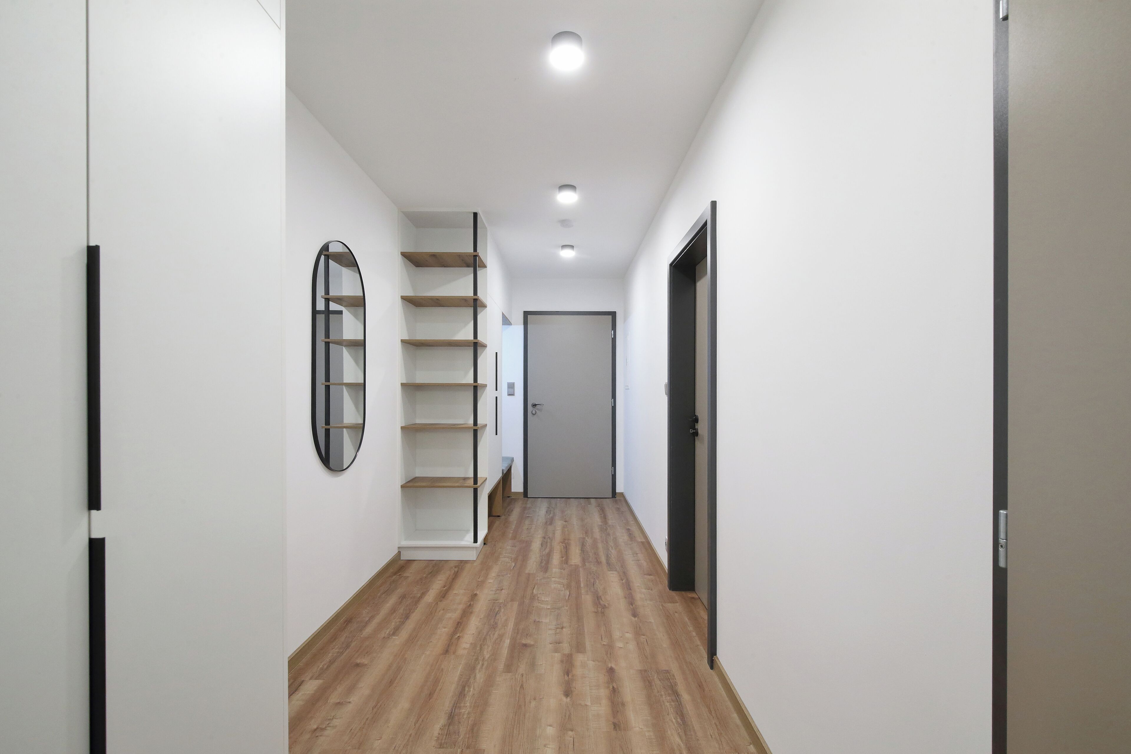 A narrow hallway with wooden flooring, white walls, and a door at the end.
