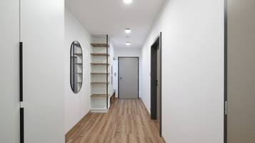 A narrow hallway with wooden flooring, white walls, and a door at the end.