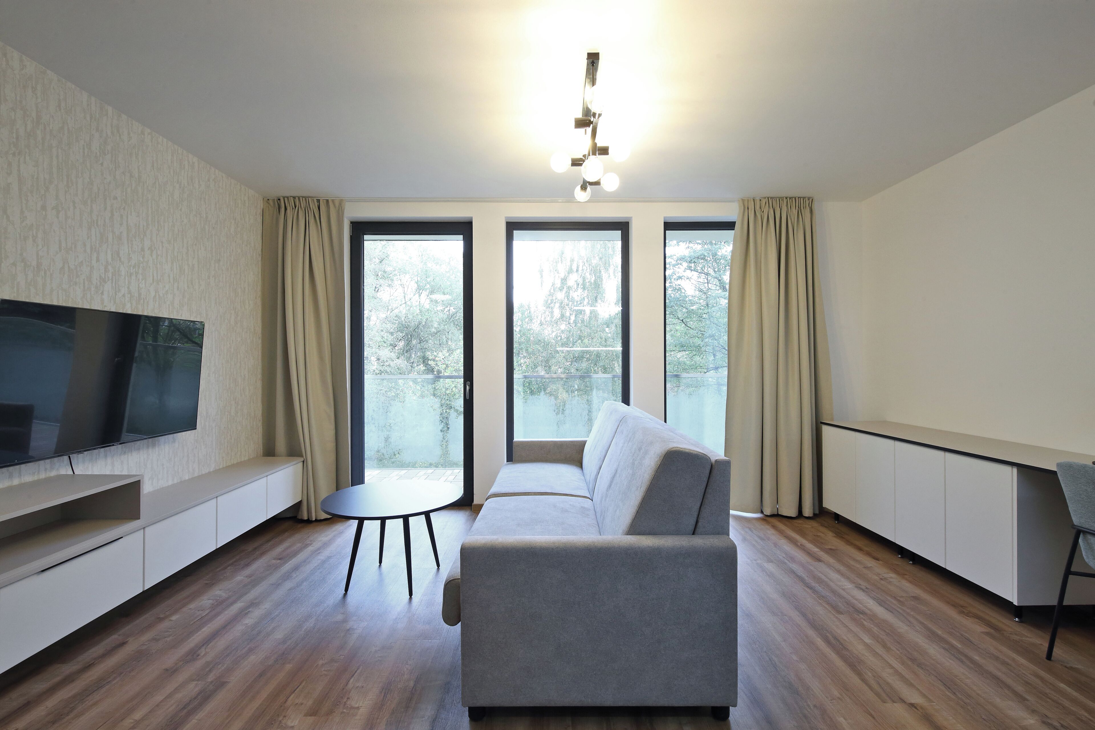 Ein modernes Wohnzimmer mit Flachbildfernseher, einer Couch, einem kleinen runden Tisch und einem Schreibtisch mit Stuhl.