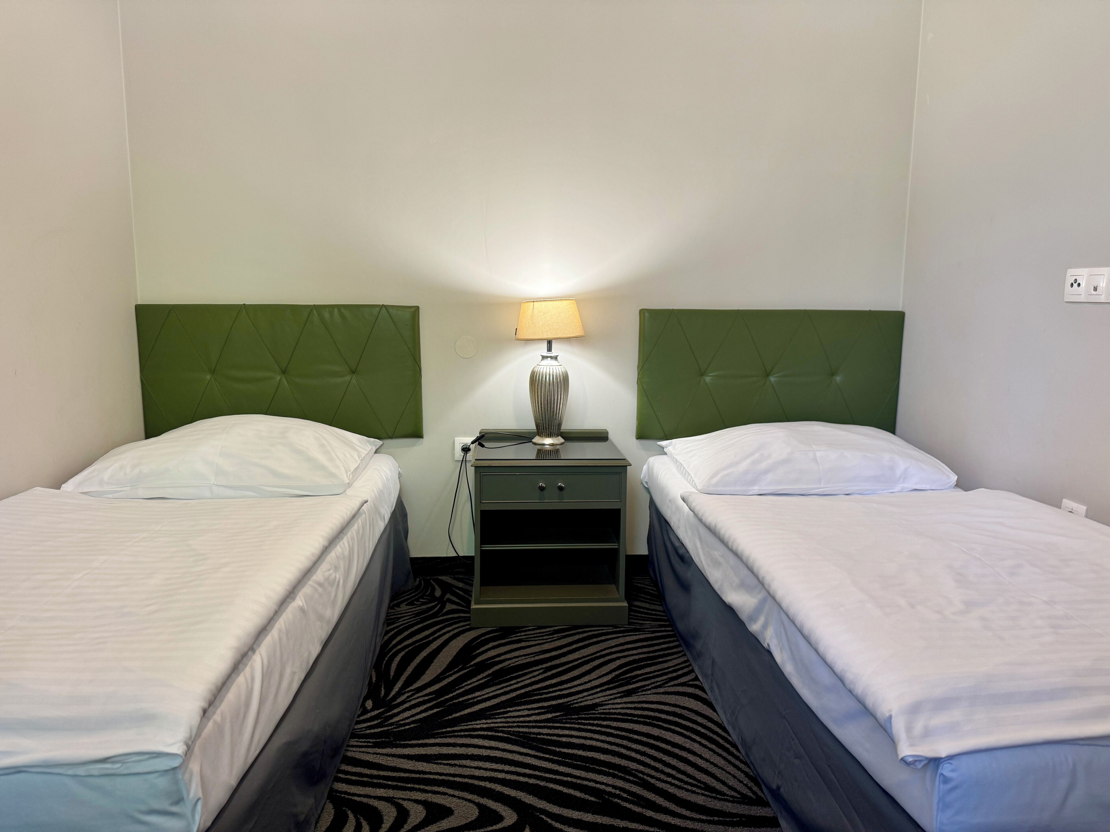 Een hotelkamer met twee bedden, een nachtkastje met een lamp en een karpet met zebraprint.