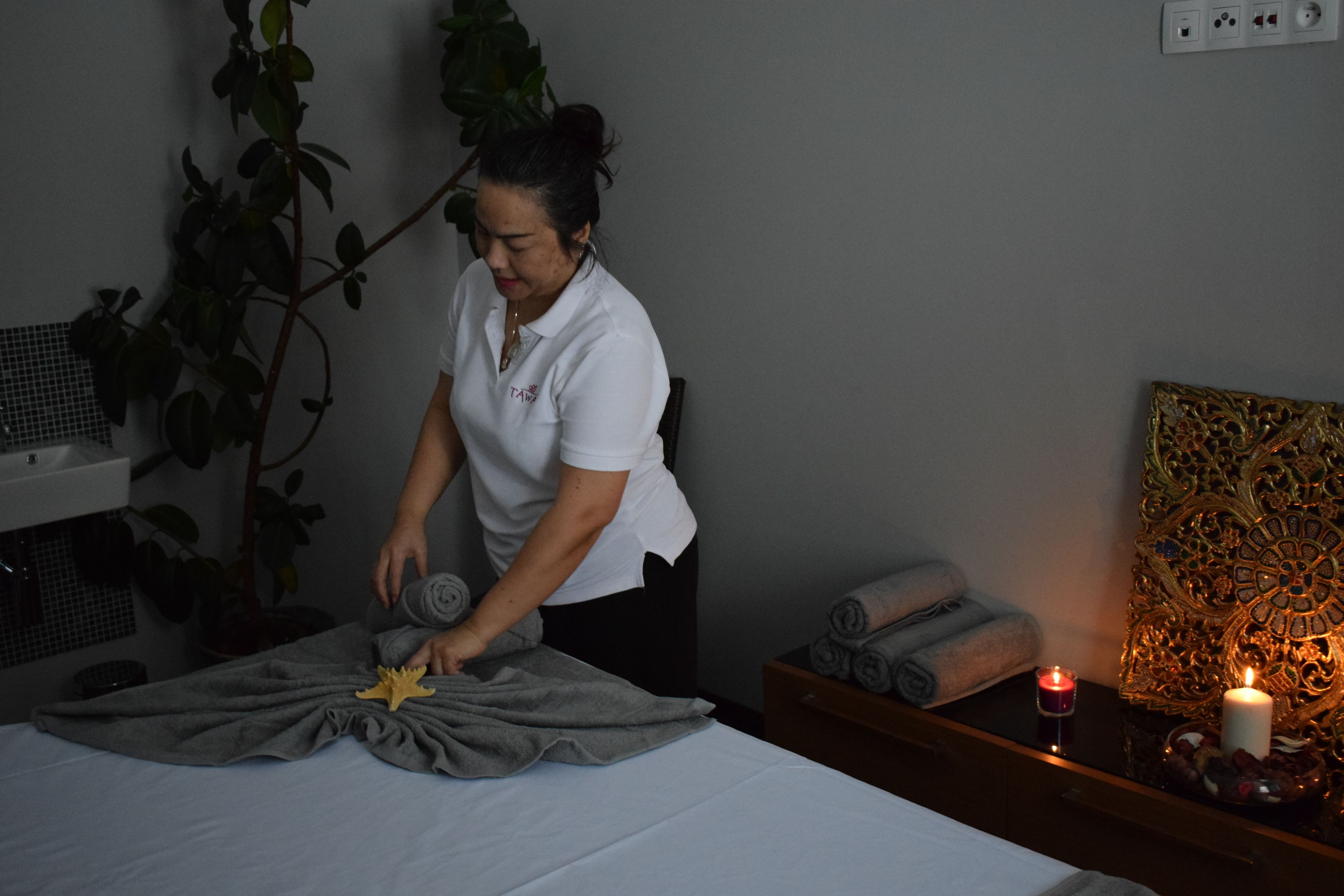 A spa room with a bed, a towel, a candle, and a decorative wall piece.