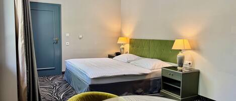 A hotel room with a bed, two bedside lamps, a nightstand, a table, and two chairs.