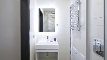 Casa de banho moderna com lavatório branco, espelho e cabine de duche em vidro.