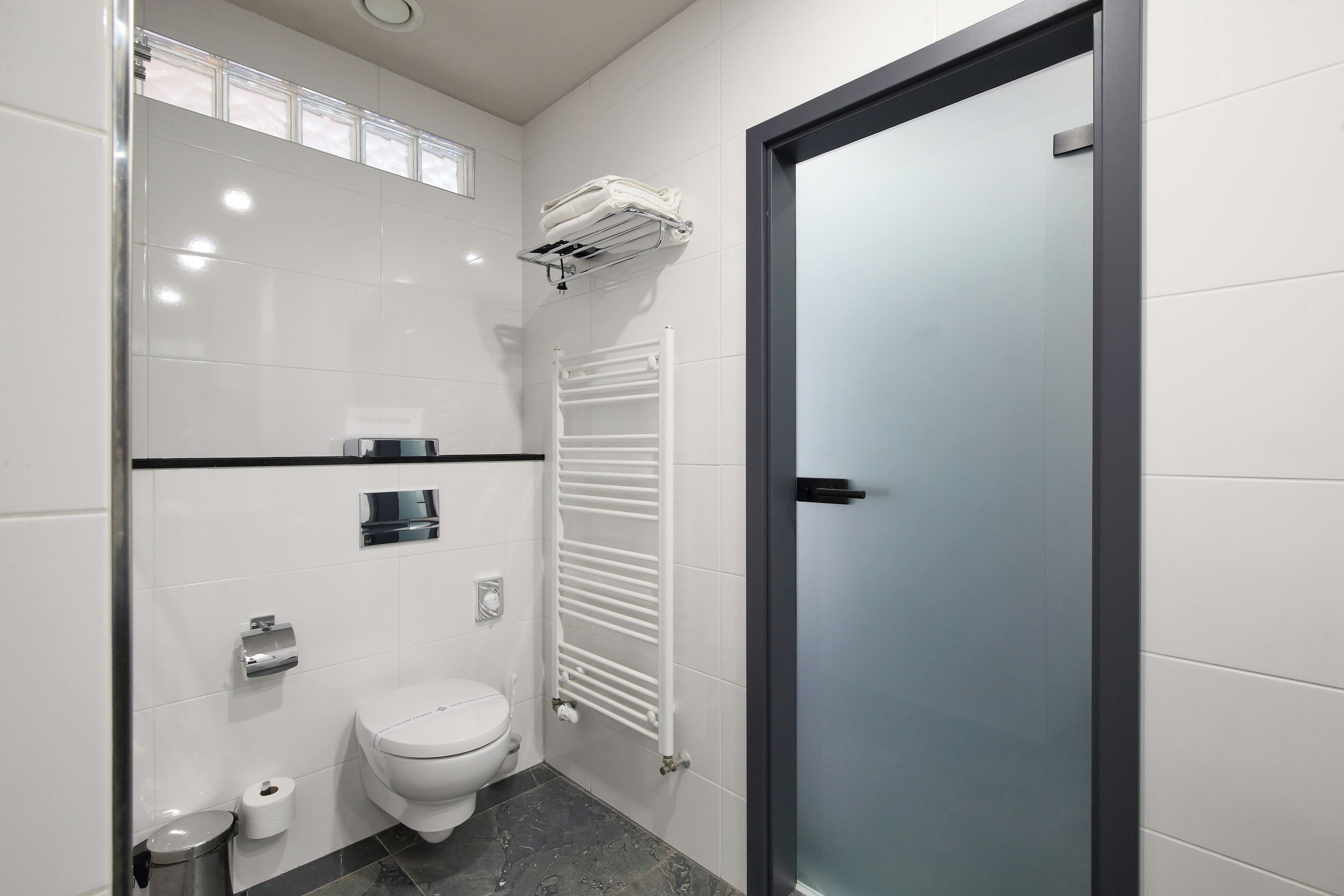 A modern bathroom with a toilet, a towel rack, a trash bin, and a glass shower enclosure.