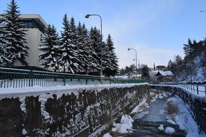Winter serenity surrounds this modern building, nestled among snow-covered trees and a tranquil stream.