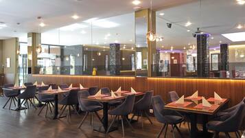A modern restaurant with a long counter, multiple tables with chairs, and a large mirror wall.