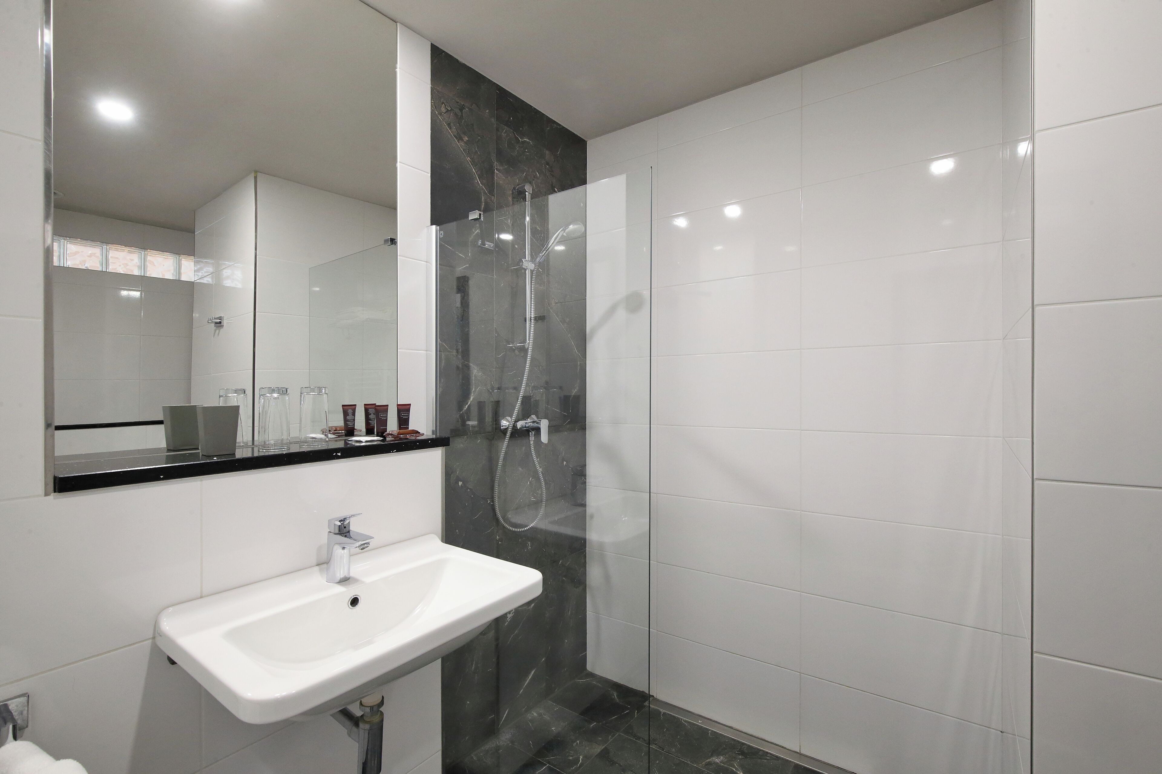 A modern bathroom with a glass-enclosed shower, a white sink, and a large mirror.