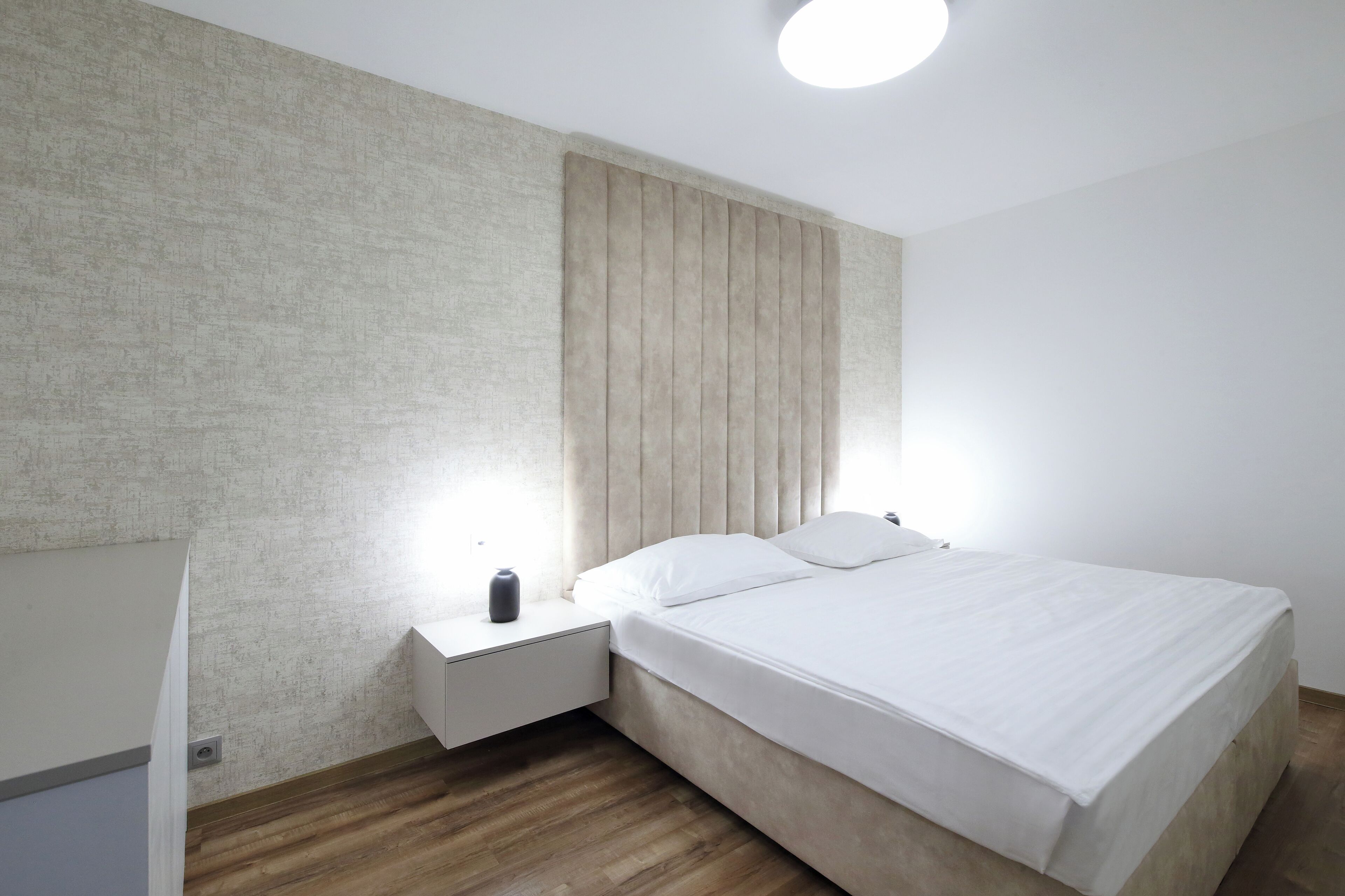 A modern bedroom with a bed, nightstand, and a wall-mounted light fixture.