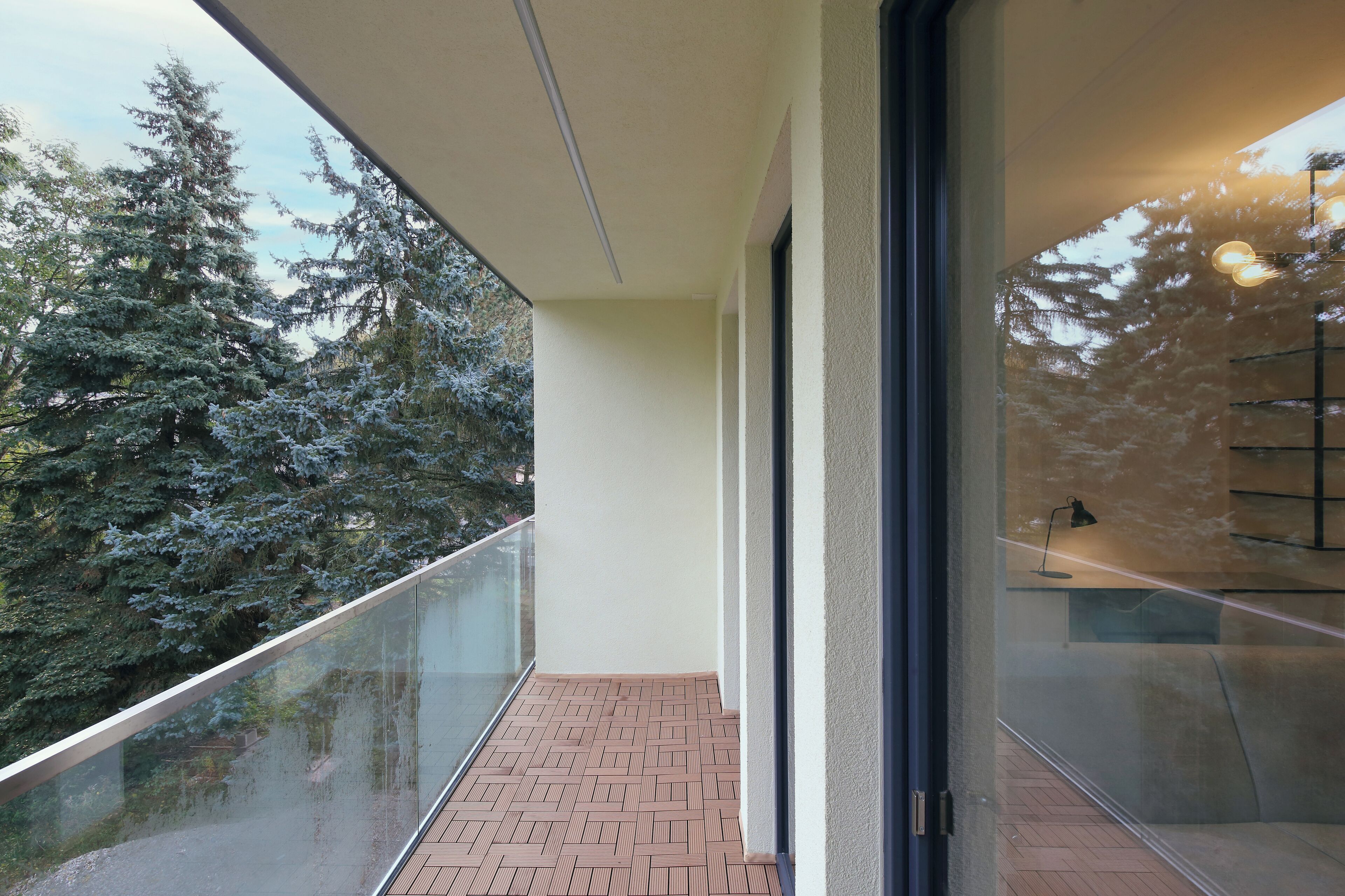 A balcony with a glass railing, a tiled floor, and a view of trees.