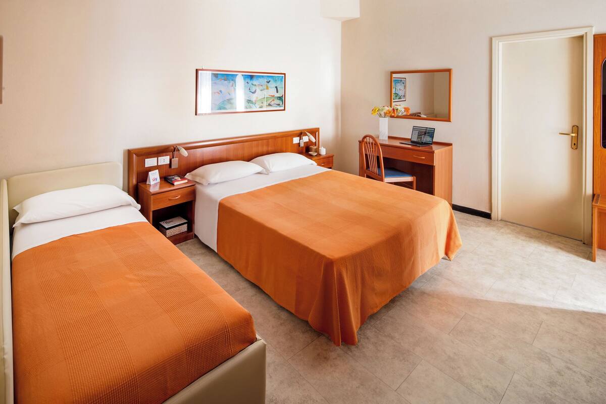 Una habitación de hotel con dos camas, un escritorio, una silla, una lámpara de escritorio, un espejo y una puerta.