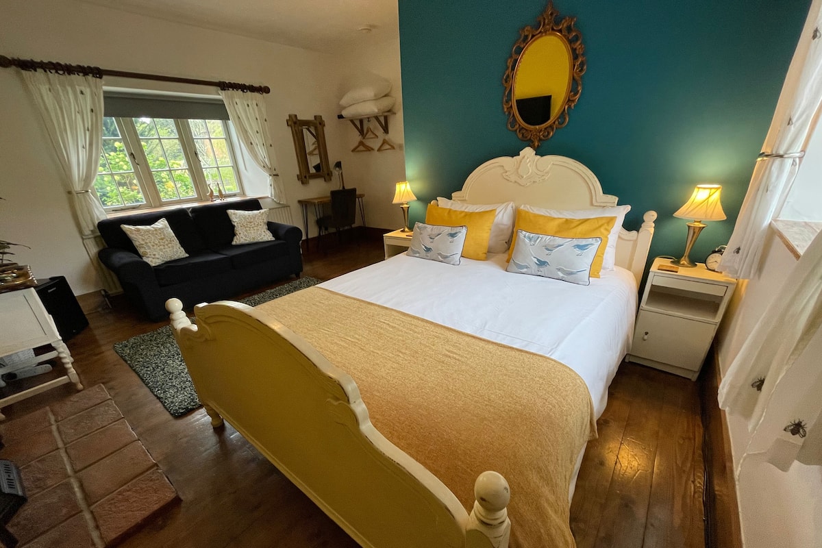 Ein Schlafzimmer mit Bett, Nachttischen, Kommode, Fenster mit Vorhängen, Spiegel und blauer Wand.