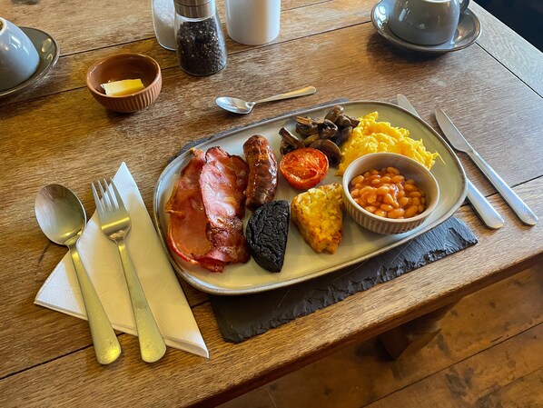 A breakfast plate with ham, sausages, mushrooms, tomatoes, scrambled eggs, baked beans, and a black pudding on a wooden table. - Home Farm Bed & Breakfast (Milton Keynes)