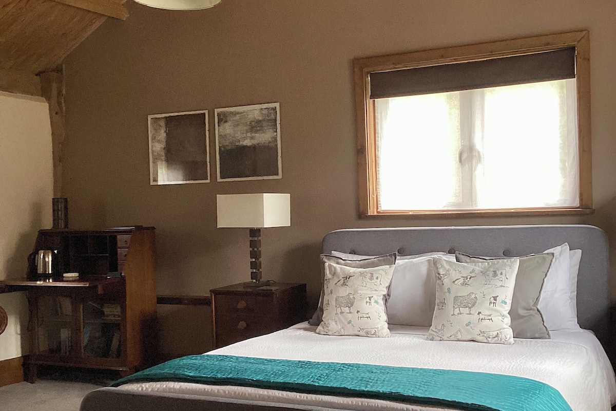 Ein Schlafzimmer mit einem großen Bett, einem Holztisch, einer Lampe und zwei Wandbildern.