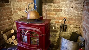 A red wood-burning stove with a kettle on top, a metal pot, and a fire poker leaning against the wall. - Home Farm Bed & Breakfast (Milton Keynes)