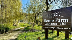 A wooden sign for Home Farm Guesthouse B&B with a pathway leading to a stone building. - Home Farm Bed & Breakfast (Milton Keynes)