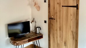 A room with a wooden desk, a television, a metal bucket, and a wooden door. - Home Farm Bed & Breakfast (Milton Keynes)