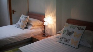 Two single beds with butterfly-patterned pillows, a bedside table with a lamp, and a wooden door in the background.