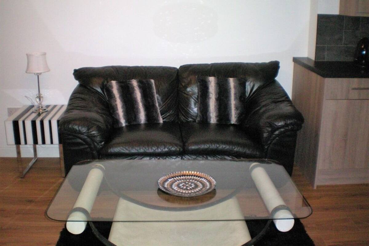 A living room with a black leather sofa, a glass coffee table with a decorative plate, and a lamp on a side table.