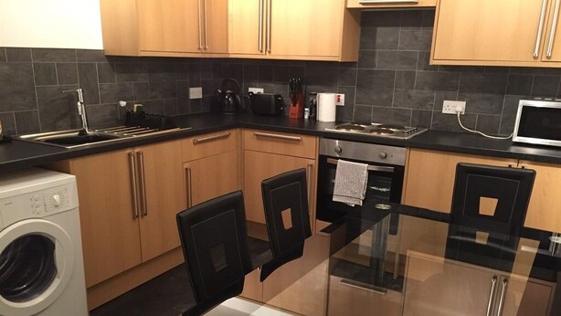 A modern kitchen with wooden cabinets, a glass dining table, and a built-in washing machine.
