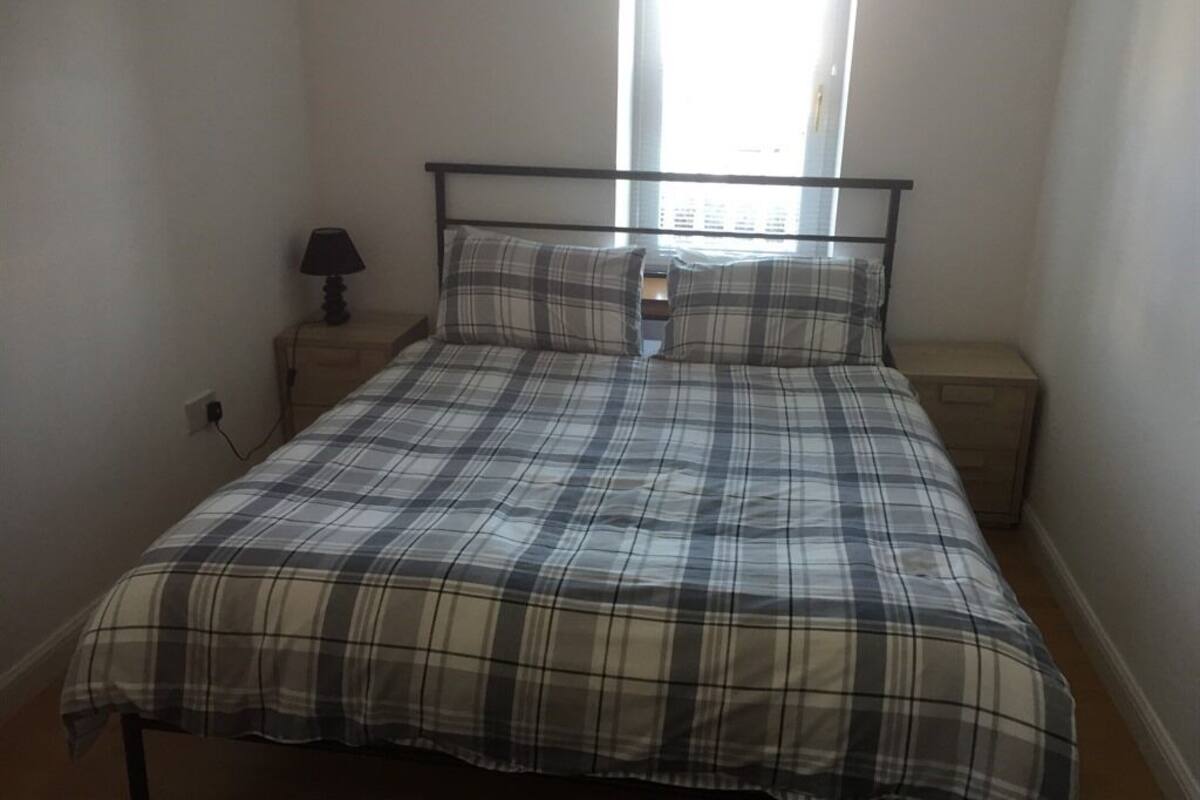 A bedroom with a bed, a nightstand, a lamp, and a window.