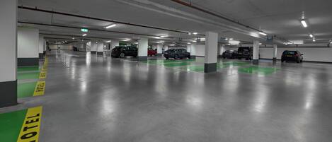 A multi-level parking garage with green and yellow parking space markings, concrete pillars, and overhead lighting.
