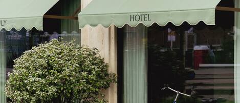 A hotel with a green awning, a potted plant, and a bicycle parked outside.