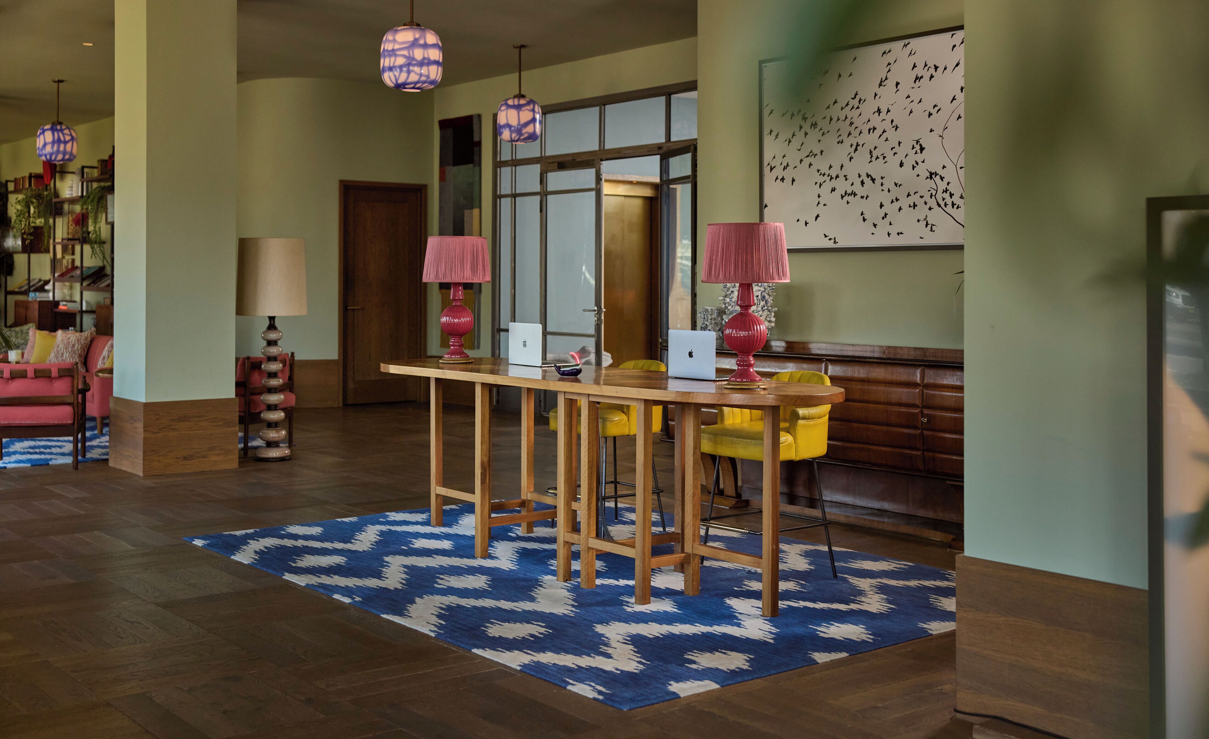 Un vestíbulo amplio con un mostrador de recepción de madera, dos sillas amarillas y una alfombra azul estampada.