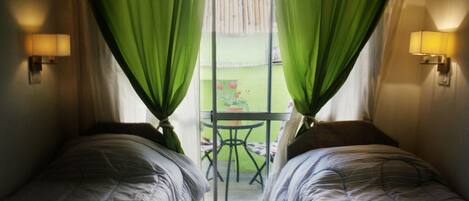 Una habitación con dos camas, una ventana con cortinas verdes, una mesa con sillas y lámparas fijadas a la pared.