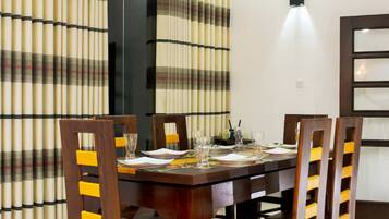 Zona pranzo con tavolo in legno apparecchiato per quattro persone, circondato da sedie con dettagli gialli.