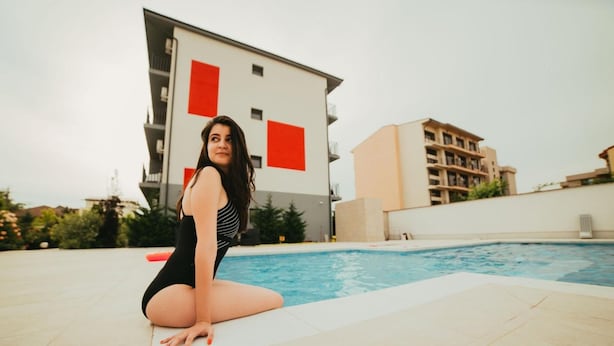 A person sitting by a swimming pool with modern buildings in the background. - Sangria Luxury Family (Navodari)