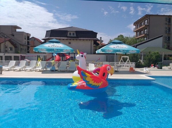 A swimming pool with a colorful inflatable flamingo float, lounge chairs, and umbrellas.