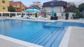 A swimming pool with lounge chairs and umbrellas, surrounded by buildings.