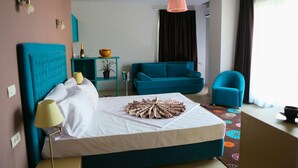 A hotel room with a bed, a teal sofa, a blue armchair, a small table with a plant, and a window with curtains. - Sangria Luxury Family (Navodari)
