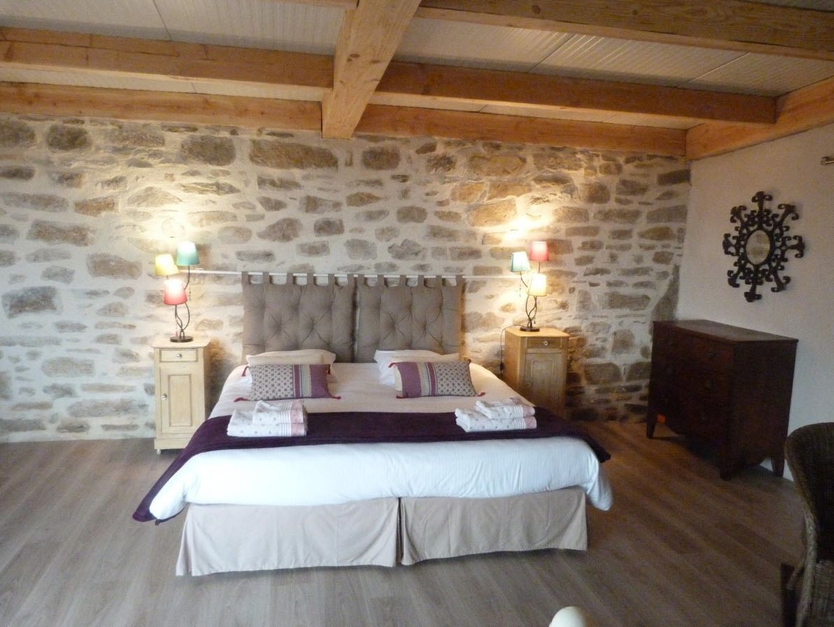A bedroom with a stone wall, a large bed with a tufted headboard, two bedside tables with lamps, and a wooden cabinet.