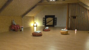 Une chambre mansardée avec un plancher en bois, un grand miroir et trois poufs.