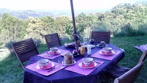 Une table à manger d’extérieur, agrémentée de sets de table, d’assiettes et de verres roses, entourée de chaises, avec une vue panoramique en arrière-plan.