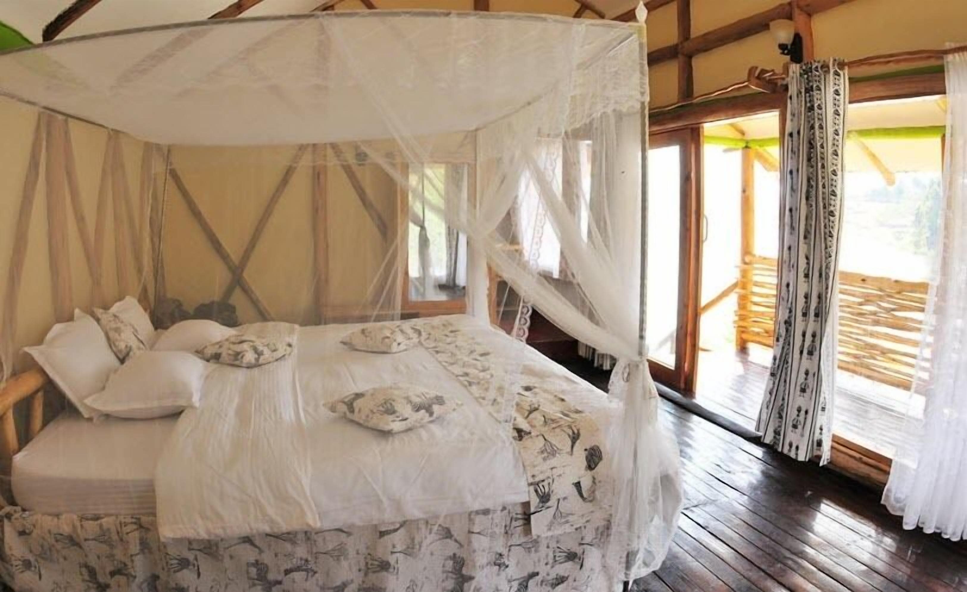 A bed with a canopy, patterned bedding, and a view of the outdoors through large windows.