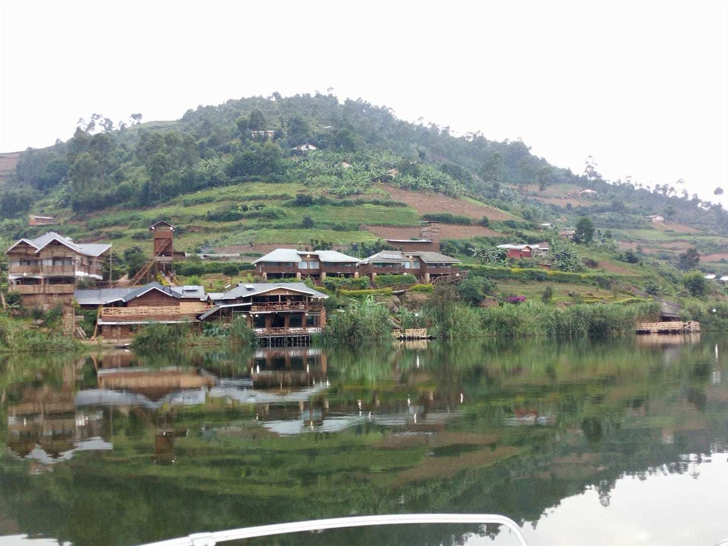 Un pueblo a orillas del lago con casas de madera construidas sobre pilotes en el agua, rodeado de exuberante vegetación y colinas.