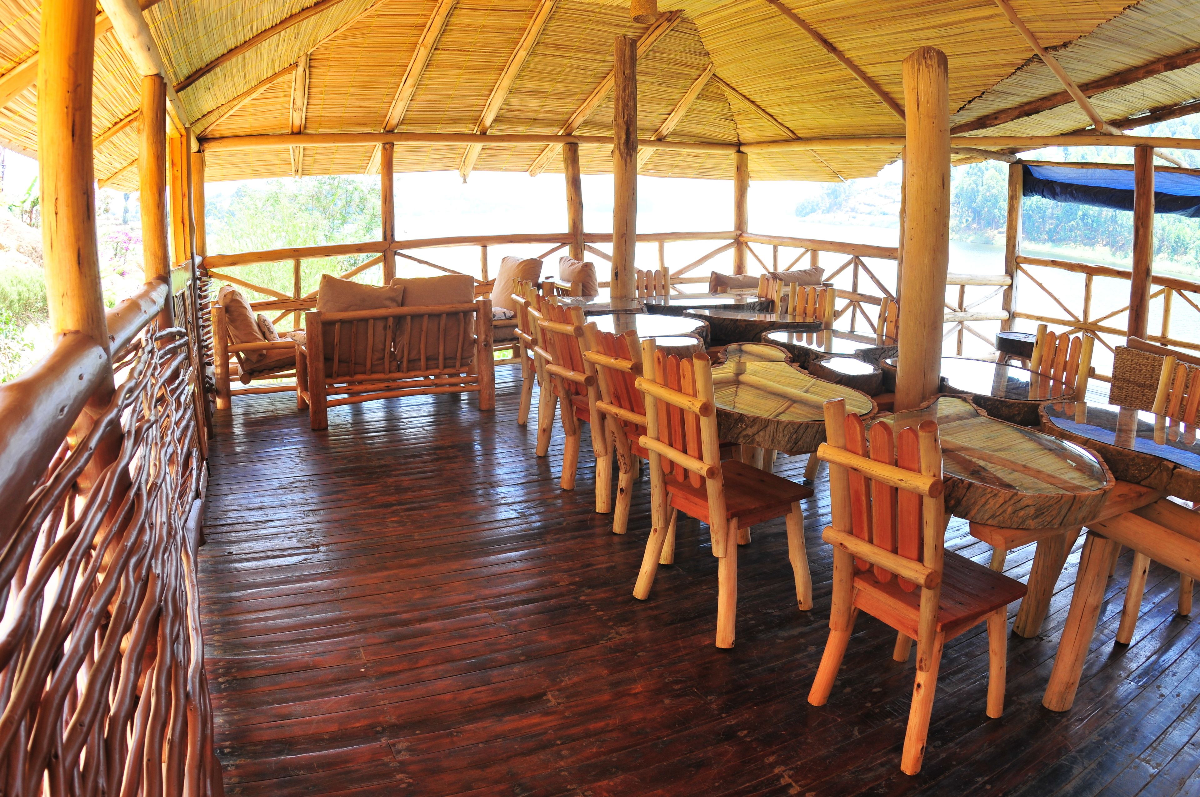 A wooden deck with tables and chairs, surrounded by a bamboo fence, overlooking a natural landscape.
