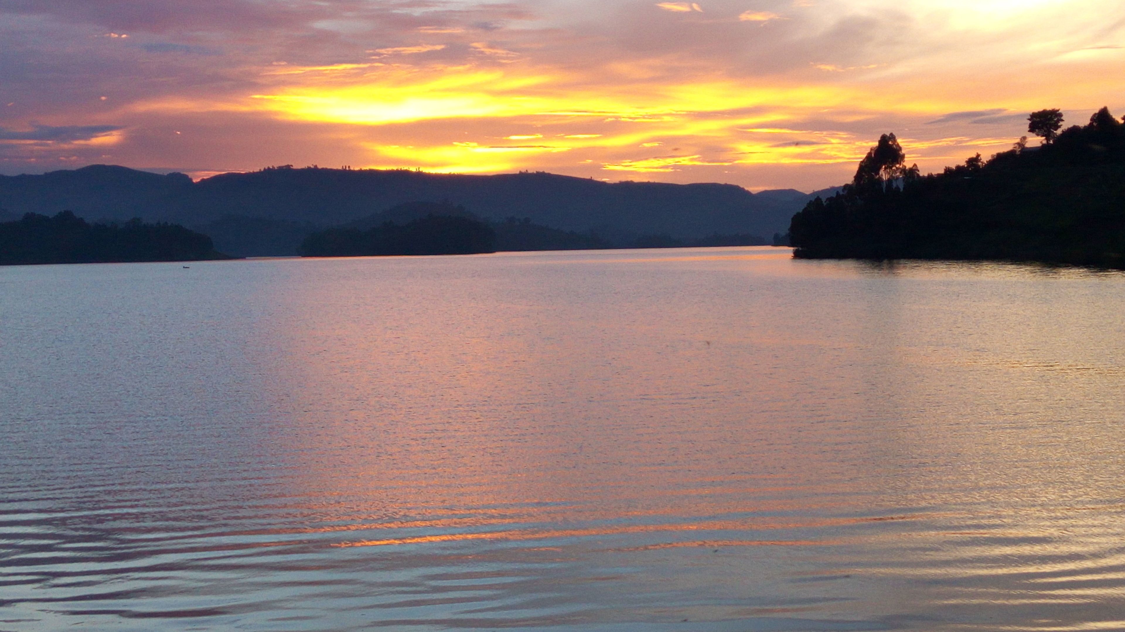 A calm lake with a sunset and mountains in the background.