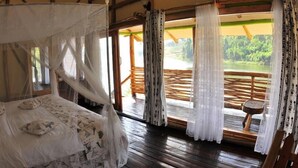 Un dormitorio con cama con dosel, suelo de madera y vistas a una terraza de madera y follaje.