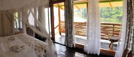 Un dormitorio con cama con dosel, suelo de madera y vistas a una terraza de madera y follaje.