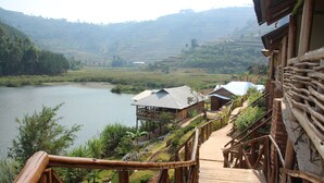 Una terraza de madera que conduce a un edificio rústico con un letrero, con vista a un lago y un paisaje montañoso.