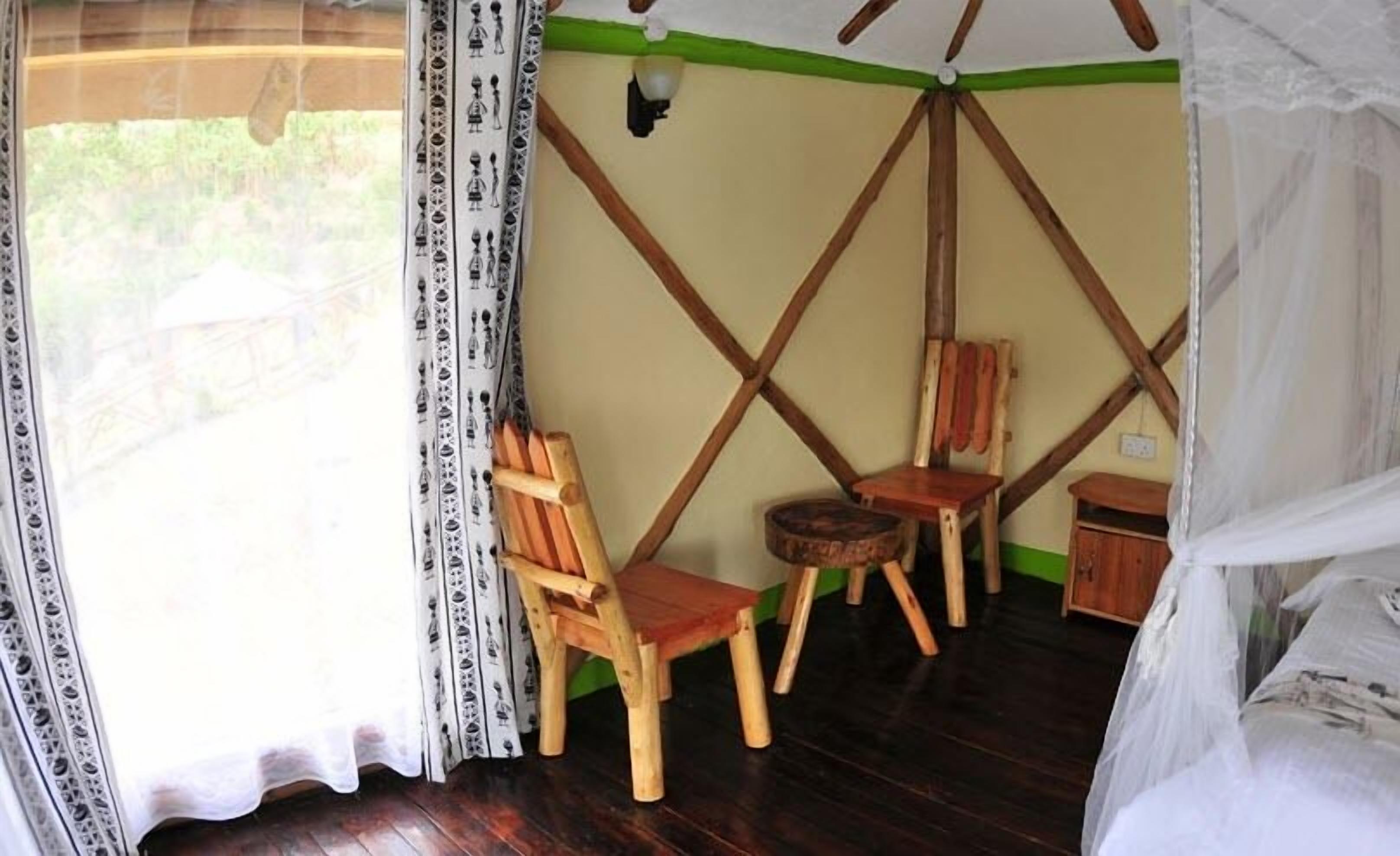 Una habitación con piso de madera, una cama con dosel, dos sillas de madera, una mesita y una pared con decoración verde y beige.