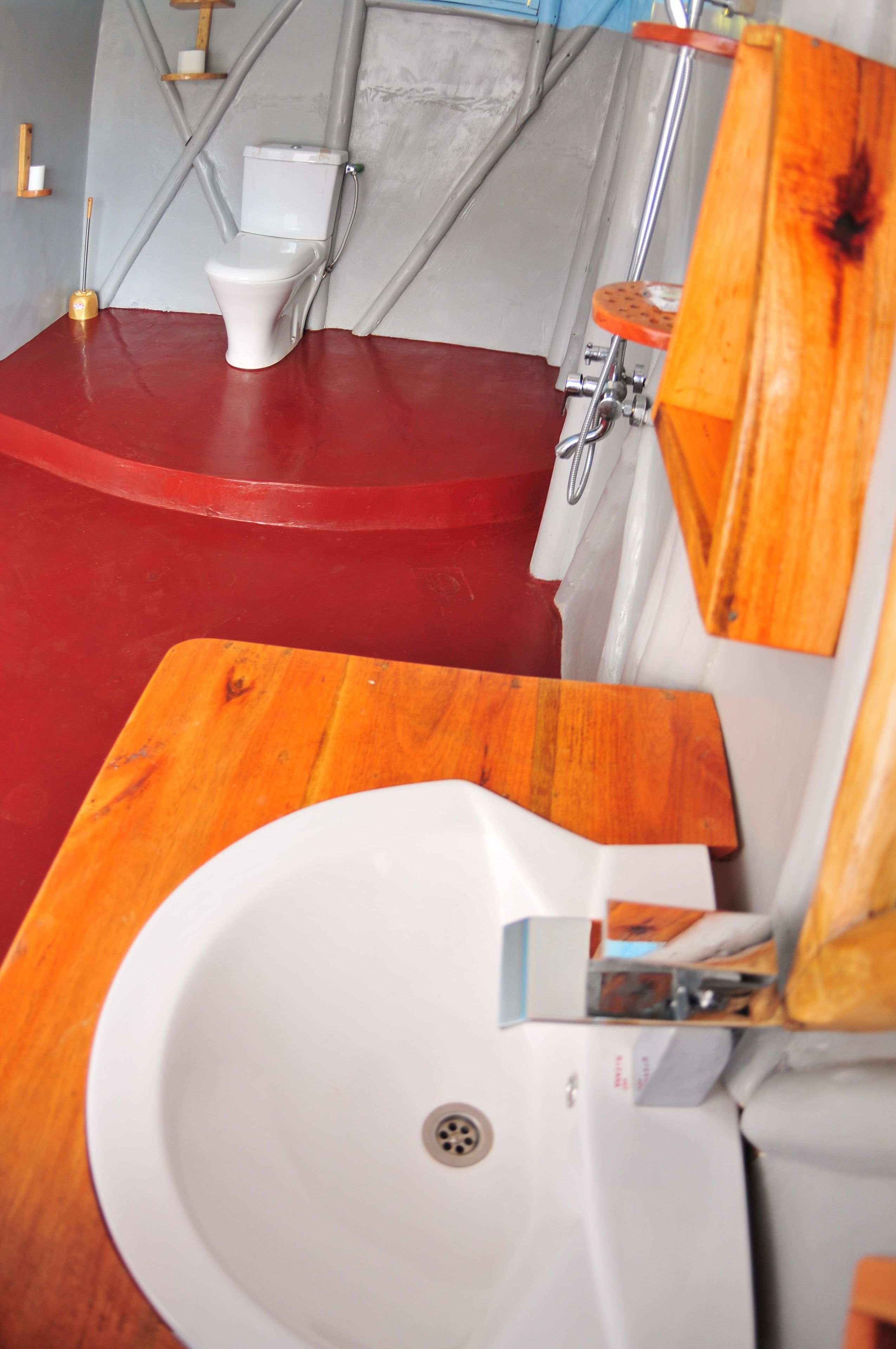 Un bagno con pavimento rosso, un WC bianco e un mobiletto da bagno in legno con lavandino.