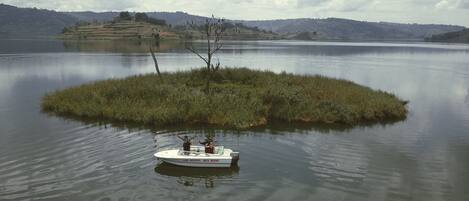 Un bote llamado "LAK BUNYONI ROCK RESORT" sobre aguas tranquilas, con una pequeña isla y colinas al fondo.
